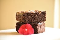 Close-up of chocolate brownies topped with nuts and a vibrant red flower.